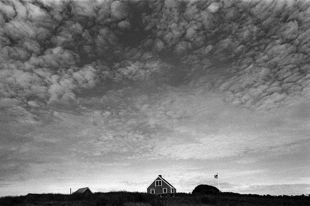 The classical barnlike structure in the middle of a field is graced by an immense cloud-strewn sky just before sunset.