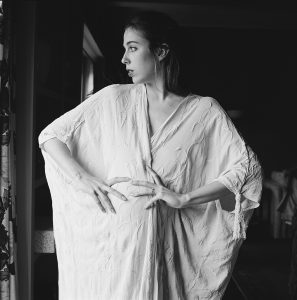 Black and white photograph of a pregnant woman in a loose garment with embroidery and a tassel hanging from the sleeve.