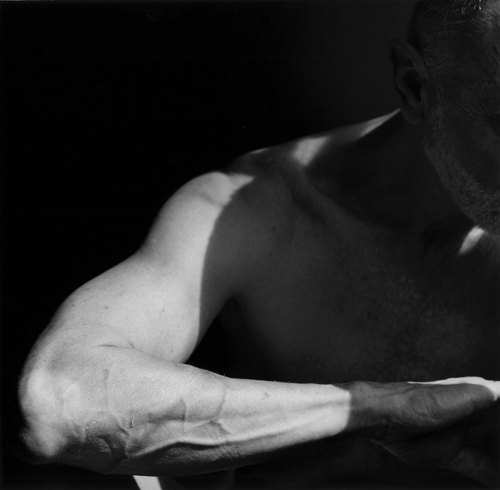 Black and white photograph of a man's arm and shoulder in shadow, with light forming wavy shapes.